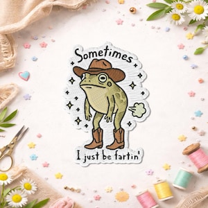 May include: Embroidered patch featuring a green frog wearing a brown cowboy hat and boots. The patch has the text "Sometimes I just be fartin'" in a playful font. The frog is depicted with a humorous expression and a puff of gas.