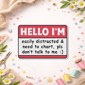 May include: A rectangular patch with a red border and the text "HELLO I'M" at the top. Below, it reads "easily distracted & need to chart, pls don't talk to me :)" in white. The patch is surrounded by sewing supplies and floral accents.