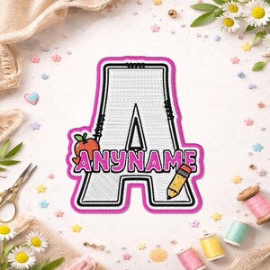 May include: A white embroidered letter A patch with a thick hot pink border. The letter features a red apple graphic on the left side and a yellow pencil graphic on the right. The text ANYNAME is embroidered in hot pink across the center.