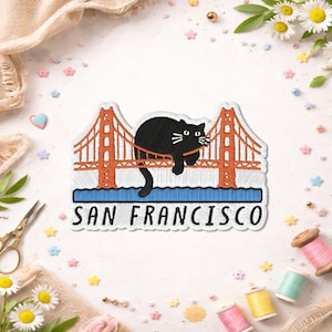 May include: Embroidered patch featuring a black cat lounging on the Golden Gate Bridge in San Francisco. The patch has orange, blue, and white details, with the city name in a bold font. A whimsical cat-themed souvenir.