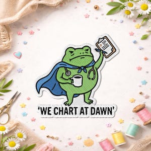 May include: Embroidered patch featuring a green frog superhero with a blue cape and stethoscope, holding a coffee mug and a clipboard. The text "WE CHART AT DAWN" is below the frog. The patch is surrounded by decorative elements.