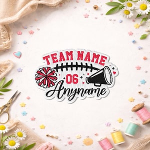 May include: An embroidered patch featuring the text TEAM NAME in red, the number 06 in red, and the text Anyname in black script. The design includes a black football lace graphic, a red and white pom-pom, and a black megaphone graphic.