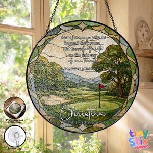 May include: A circular stained glass suncatcher featuring a golf course landscape with a large tree and a red flag. The text reads: Some journeys take us beyond the course... but leave footprints on the fairway of our hearts. IN LOVING MEMORY OF Christina 11/4/1968 5/8/2026.