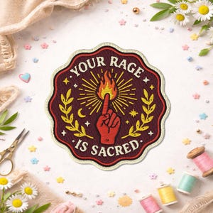 May include: Embroidered patch with the text "YOUR RAGE IS SACRED". The patch features a red hand pointing upwards with a flame at the fingertip, surrounded by a sunburst design and laurel leaves. The patch has a burgundy border.