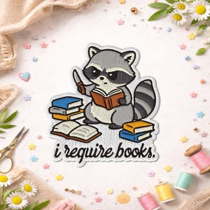 May include: Embroidered patch featuring a gray raccoon holding a knife and reading a book. The raccoon is surrounded by stacks of books and the text "i require books." The patch has a white border and is suitable for jackets, bags, or other fabric items.