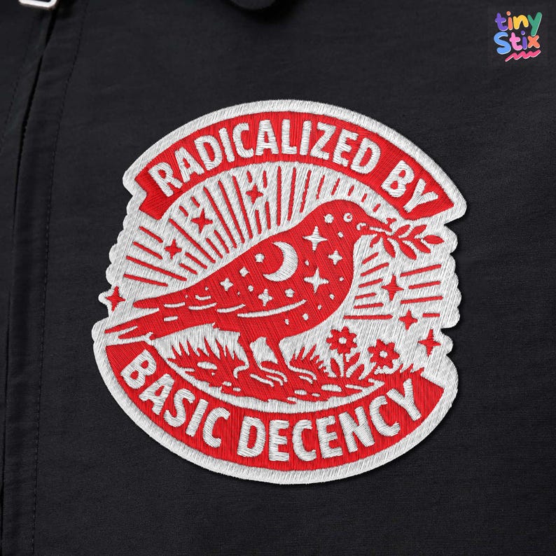 May include: Embroidered patch with the text "RADICALIZED BY BASIC DECENCY" in red and white. The patch features a red bird carrying a sprig, surrounded by stars, a crescent moon, and flowers. The patch is on a black background.