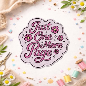 May include: Embroidered patch with the text "Just One More Page" in pink script, surrounded by pink flowers and diamonds. The patch has a light pink background and a black border. Perfect for book lovers.