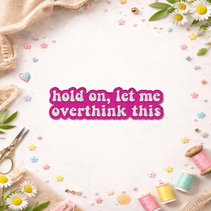 May include: A pink embroidered patch with the text "hold on, let me overthink this" in white. The patch is surrounded by sewing supplies, including spools of thread, scissors, and decorative elements like flowers and stars.