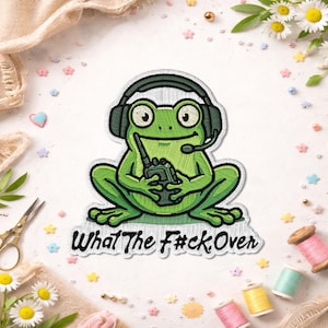 May include: Embroidered patch of a green frog wearing a headset and holding a walkie-talkie. The frog has large eyes and is sitting with its legs spread. The text "What The F#ck Over" is below the frog.