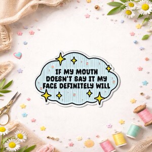 May include: A light blue cloud-shaped embroidered patch featuring the black text IF MY MOUTH DOESN'T SAY IT MY FACE DEFINITELY WILL, accented with yellow four-pointed star icons. The patch has a white border and a textured fabric appearance.