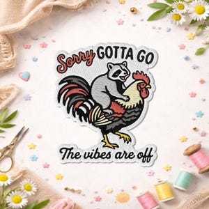 May include: Embroidered patch featuring a raccoon riding a rooster, with the text "Sorry Gotta Go" and "The vibes are off". The patch has a white border and is decorated with colorful thread.
