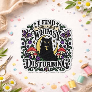 May include: An embroidered patch featuring a black cat sitting in front of a yellow crescent moon. The text reads I FIND YOUR LACK OF WHIMSY DISTURBING. The design includes purple butterflies, red and white mushrooms, and green vines on a white background.