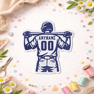 May include: A navy blue embroidered patch featuring a baseball player holding a bat across his shoulders. The jersey displays "ANYNAME" above the number "00". The patch is surrounded by white stitching.