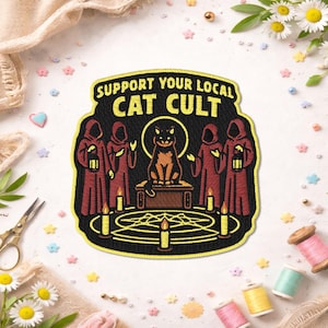 May include: Embroidered patch with the text "SUPPORT YOUR LOCAL CAT CULT". The patch features a black cat on a table, surrounded by figures in red robes, candles, and a pentagram design. The patch is black with yellow and red accents.