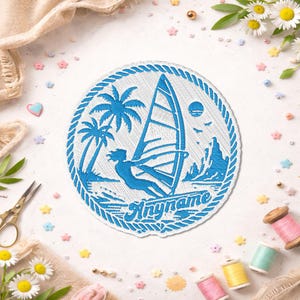 Peut inclure: Un écusson brodé circulaire présentant un motif bleu représentant une personne faisant de la planche à voile près de palmiers et de montagnes, entouré d'une bordure en corde. Le mot "Anyname" est brodé en bleu sur le fond en tissu blanc.