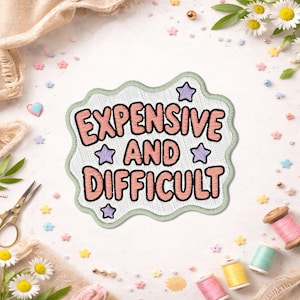 May include: An embroidered patch with a wavy light green border and a white background. The text reads EXPENSIVE AND DIFFICULT in bold, rounded, salmon-colored letters. Four small, light purple stars are scattered around the text.