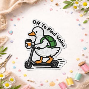Peut inclure: Écusson brodé représentant un canard blanc sur un scooter noir, avec un sac à dos vert et une tasse de café. Le texte "Off To Find Veins" est en noir. Le design est sur fond blanc, avec des éléments décoratifs.