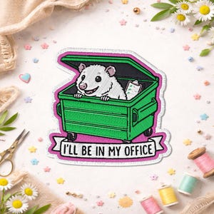 May include: Embroidered patch featuring a cartoon opossum in a green dumpster with the text "I'll be in my office." The patch has a pink border and is surrounded by craft supplies and flowers.