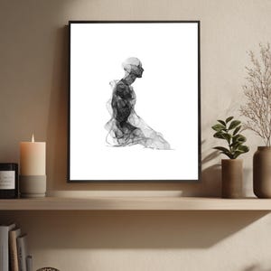 Puede incluir: Impresión artística abstracta en blanco y negro que representa una figura arrodillada. La obra de arte está enmarcada en un borde negro y se exhibe en una estantería de madera. La imagen incluye una vela, libros y plantas decorativas.