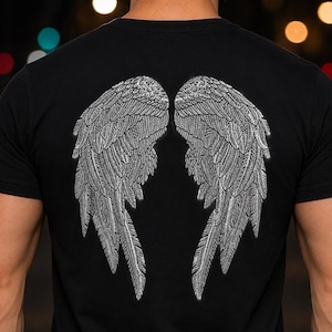 Może przedstawiać: Czarny t-shirt z kr&oacute;tkim rękawem z dużą, szczeg&oacute;łową grafiką dw&oacute;ch symetrycznych skrzydeł anioła na plecach. Skrzydła wykonane są w teksturowanym, mieniącym się srebrnym kolorze ze skomplikowanymi wzorami pi&oacute;r na całej powierzchni.