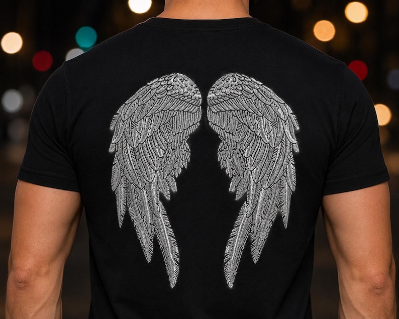 Może przedstawiać: Czarny t-shirt z kr&oacute;tkim rękawem z dużą, szczeg&oacute;łową grafiką dw&oacute;ch symetrycznych skrzydeł anioła na plecach. Skrzydła wykonane są w teksturowanym, mieniącym się srebrnym kolorze ze skomplikowanymi wzorami pi&oacute;r na całej powierzchni.