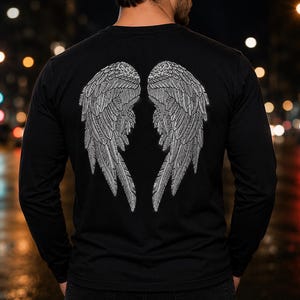 Op de afbeelding: Een zwart shirt met lange mouwen voorzien van een grote, gedetailleerde afbeelding van twee witte gevederde vleugels in het midden van de rug. De vleugels zijn weergegeven met ingewikkelde lijnen, die individuele veren en een symmetrisch ontwerp tonen.