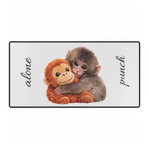 Puede incluir: Una alfombra rectangular blanca con borde negro presenta dos monos de peluche abrazándose. Uno es marrón y el otro naranja. La palabra "alone" está a la izquierda y "punch" a la derecha.