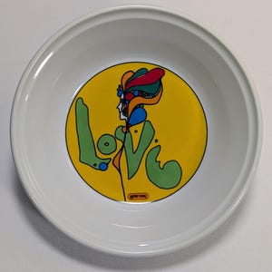 May include: White ceramic bowl with a vibrant illustration. The design features a yellow circle with a colorful profile and the word "LOVE" in green. The artist's signature, "peter max", is at the bottom.
