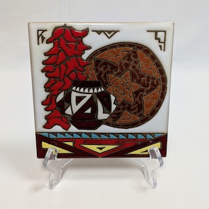 May include: A square ceramic tile featuring a vibrant illustration of a red chili pepper ristra, a patterned clay pot, and a woven basket. The lower section displays a geometric border in red, yellow, and light blue against a white background.