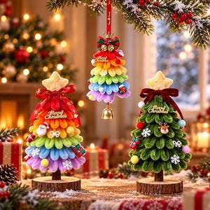 Puede incluir: Dos adornos de árbol de Navidad de mesa y uno colgante. Los árboles están hechos de bucles de tela coloridos en capas con una estrella en la punta, un lazo rojo y el texto Merry Christmas. Incluyen pequeños adornos festivos.