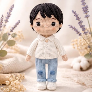 May include: A handmade crochet doll of a boy with black hair, wearing a white jacket, blue pants, and white shoes. The doll has large, expressive eyes and is standing in front of a soft, blurred background with lavender sprigs and other decorative elements.