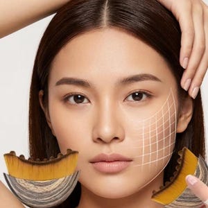 May include: A woman's face with a grid overlay, showcasing two makeup brushes. The brushes have a unique design with a curved, fan-like shape, featuring a blend of yellow and brown bristles and a marbled handle.