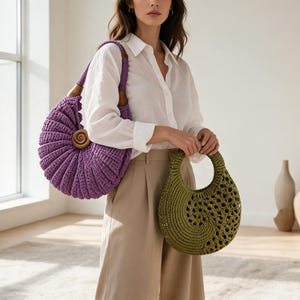 Puede incluir: Un bolso de ganchillo morado de forma circular con un detalle de espiral de madera, junto a un bolso de ganchillo verde oliva m&aacute;s peque&ntilde;o con patr&oacute;n calado y asa circular, portados con una camisa blanca y pantalones de color beige.