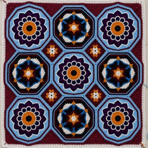Könnte beinhalten: Eine quadratische Häkeldecke mit einem sich wiederholenden Muster aus großen achteckigen Motiven in Dunkelburgunder, leuchtendem Orange, Hellblau, Dunkellila und Weiß. Das Design umfasst komplexe blumenartige Formen und kleine Sternakzente.