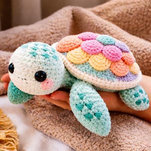 May include: A handmade crochet turtle in pastel shades. The turtle features a light blue head and limbs, a shell with rainbow-coloured scales, and large black eyes. The turtle is approximately 15 cm long.