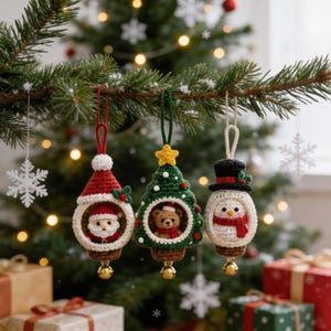 Könnte beinhalten: Drei gehäkelte Weihnachtsanhänger hängen an einem Zweig. Der erste ist ein Weihnachtsmann mit roter Mütze, der zweite ein grüner Weihnachtsbaum mit Teddybär und der dritte ein Schneemann mit schwarzem Zylinder. Jeder Anhänger hat unten eine kleine goldene Glocke.