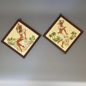 May include: Two framed wall art pieces with a tropical theme. Each features a dancing figure in a colorful outfit against a yellow background, palm trees, and a wooden frame. One figure plays a drum.