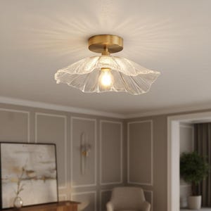 May include: A ceiling light with a brass fitting and a clear, petal-shaped glass shade. The light bulb is visible, emitting a warm glow. The fixture is mounted on a white ceiling.