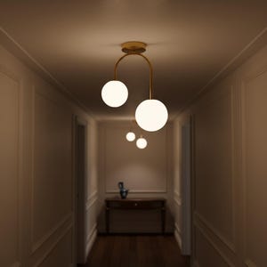 May include: A hallway featuring modern pendant lighting. Each light has a spherical, white glass globe hanging from a gold-coloured metal fixture. The lights are arranged in a line, creating a sense of depth and perspective.