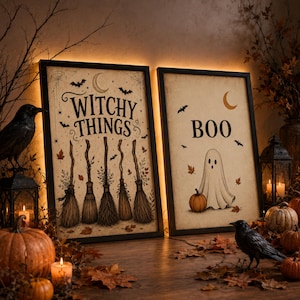 May include: Two framed rectangular wall art prints with a cream background. The left print features the text "WITCHY THINGS" above five illustrated broomsticks, bats, and a crescent moon. The right print displays the text "BOO" with a ghost and a pumpkin.