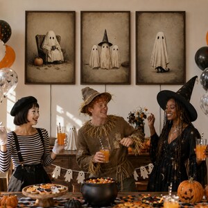 Puede incluir: Tres cuadros de pared con ilustraciones de fantasmas cuelgan sobre una mesa con tres personas disfrazadas de Halloween. La mesa contiene un caldero negro lleno de dulces, una bandeja de madera con galletas y calabazas naranjas.