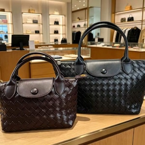 May include: Two woven handbags with top handles and a front flap closure featuring a single button. The smaller bag is dark brown, while the larger bag is black. Both bags have a distinct woven texture across the body and smooth leather accents.