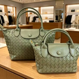 May include: Two sage green handbags featuring a woven leather exterior pattern. Each bag includes dual top handles, a front flap with a single button closure, and a zippered main compartment. The bags are displayed in a larger and smaller size.