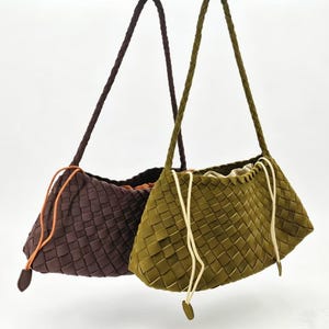 Puede incluir: Dos bolsos de hombro tejidos. Uno es de color marrón oscuro con un cordón naranja, y el otro es verde oliva con un cordón crema. Ambos bolsos tienen correas trenzadas y un diseño de tejido de cesta.
