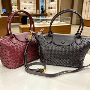 May include: Two woven handbags, one in deep burgundy and one in black, featuring a top handle, a fold-over flap with a snap button closure, a gold-tone zipper, and a detachable, adjustable shoulder strap with gold-tone hardware and a buckle.