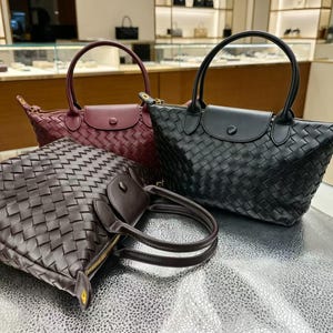 May include: Three handbags featuring a woven exterior pattern, each with two top handles, a zippered closure, and a flap with a snap button. The collection includes one black bag, one burgundy bag, and one dark brown bag, all with gold-tone hardware.