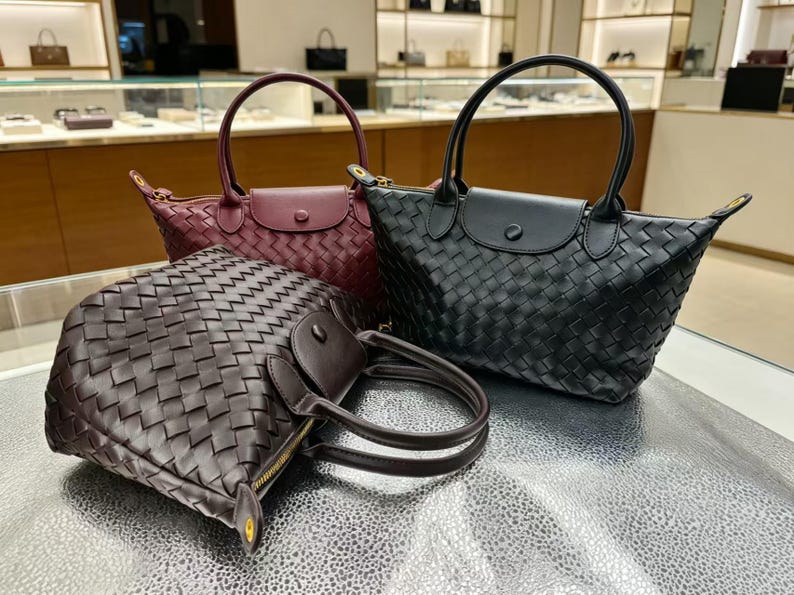 May include: Three handbags featuring a woven exterior pattern, each with two top handles, a zippered closure, and a flap with a snap button. The collection includes one black bag, one burgundy bag, and one dark brown bag, all with gold-tone hardware.
