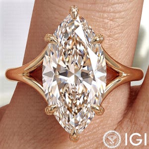 Pode incluir: Um anel de diamante com corte marquise e banda de ouro. O diamante é cravejado com garras de ouro e tem um corte brilhante. O anel está em um dedo, mostrando o design intrincado e o brilho da pedra preciosa.