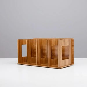 May include: A wooden desk organiser with four compartments. The organiser is made of light brown wood and has a rectangular shape. Each compartment has a square cutout on the front for easy access. It sits on a white surface.