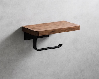 May include: A modern bathroom accessory featuring a wooden shelf and a black metal toilet paper holder. The shelf is made of light brown wood, and the holder has a curved design. The fixture is mounted on a light gray wall.